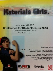 WoPhy11 Program Cover read Material Girls and shows a UNL student dressed and posed as Rosie the Riveter against a white background with yellow edge.